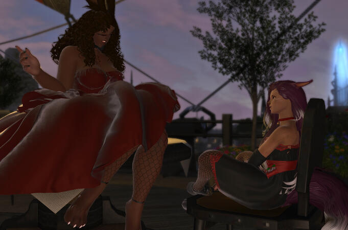 Emery and Lili'a are having a conversation at a diner. Emery is sitting on a table while Lili is on a large chair. Emery is wearing a long, cold shoulder, red dress and fishnet tights. Lili is wearing a black dress with red accents, a red bell collar.
