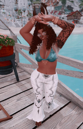 Emery is posed on a dock in the Mist housing district. She is wearing a turquoise bikini top with white bell bottom pants. Their hands are up in the air to shield their face from the light rain. She is smiling at the camera.