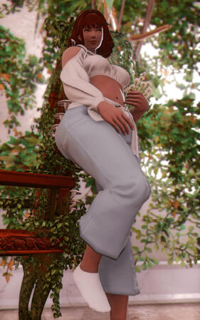 Ione is posed idly by a chair overgrown with ivy. She is wearing casual loungewear. She is holding a bundle of white clover flower and smiling, looking at something off camera. There is ivy on the walls behind her with light bleeding through.